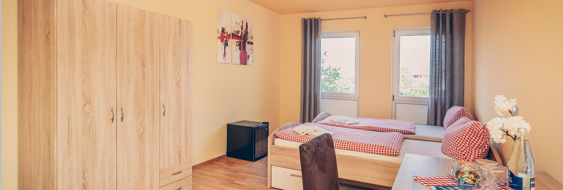 Blick in ein Zimmer des Friederike-Wackler-Gästehauses mit Bett, Schrank sowie einem Tisch mit Getränken und Snacks.